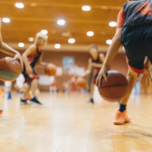 Børn i farverigt basketball tøj træner boldkontrol i sportshal – ideelt outfit til aktive børn med interesse for basketball.
