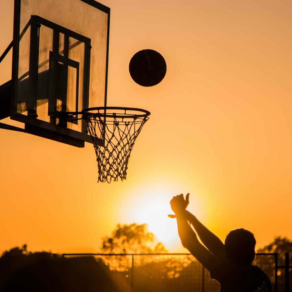 Barn skyder til basketballkurv i solnedgang – ideel inspiration til basketball tøj til børn og udendørs aktivitet.