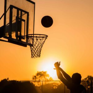 Barn skyder til basketballkurv i solnedgang – ideel inspiration til basketball tøj til børn og udendørs aktivitet.