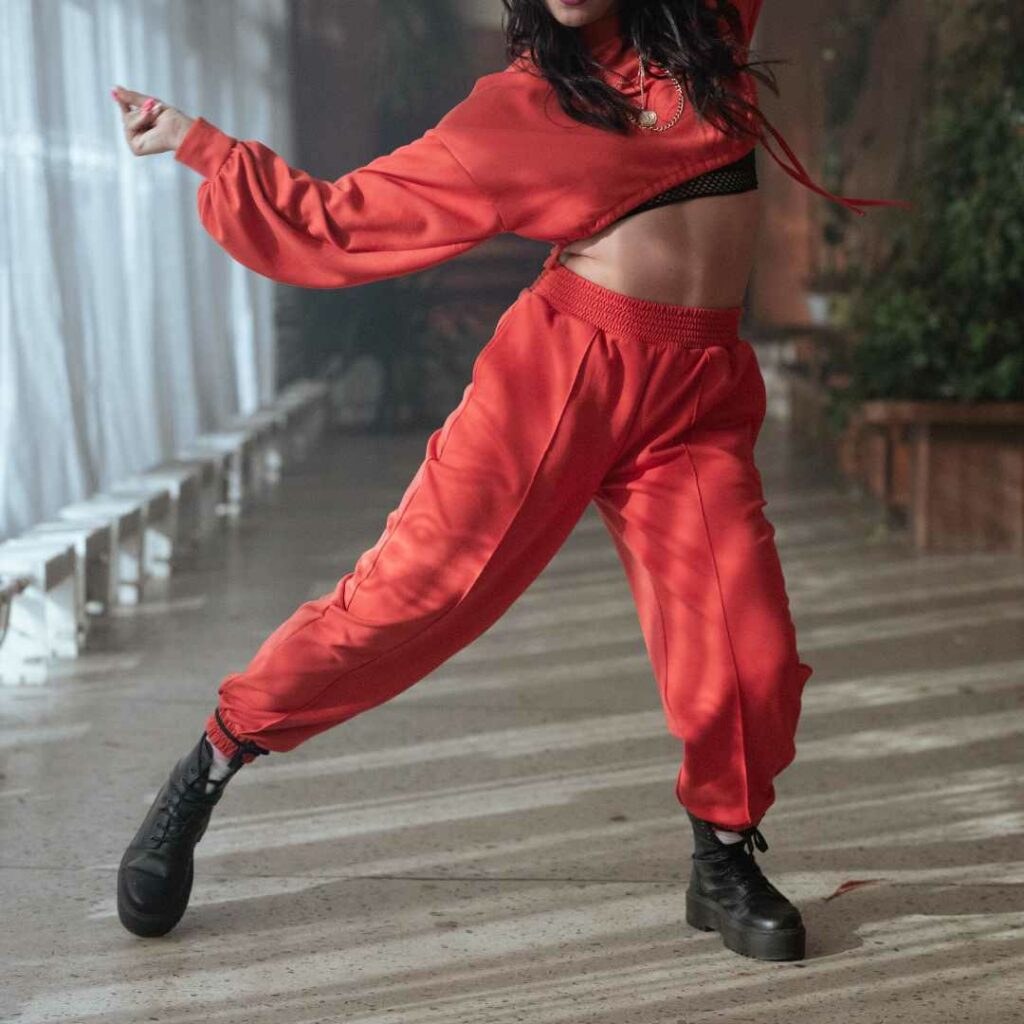 Kvinde i rød cropped sweatshirt og matchende joggingbukser i bevægelse under dans – sporty og energisk look i rødt outfit.