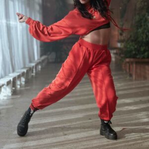 Kvinde i rød cropped sweatshirt og matchende joggingbukser i bevægelse under dans – sporty og energisk look i rødt outfit.